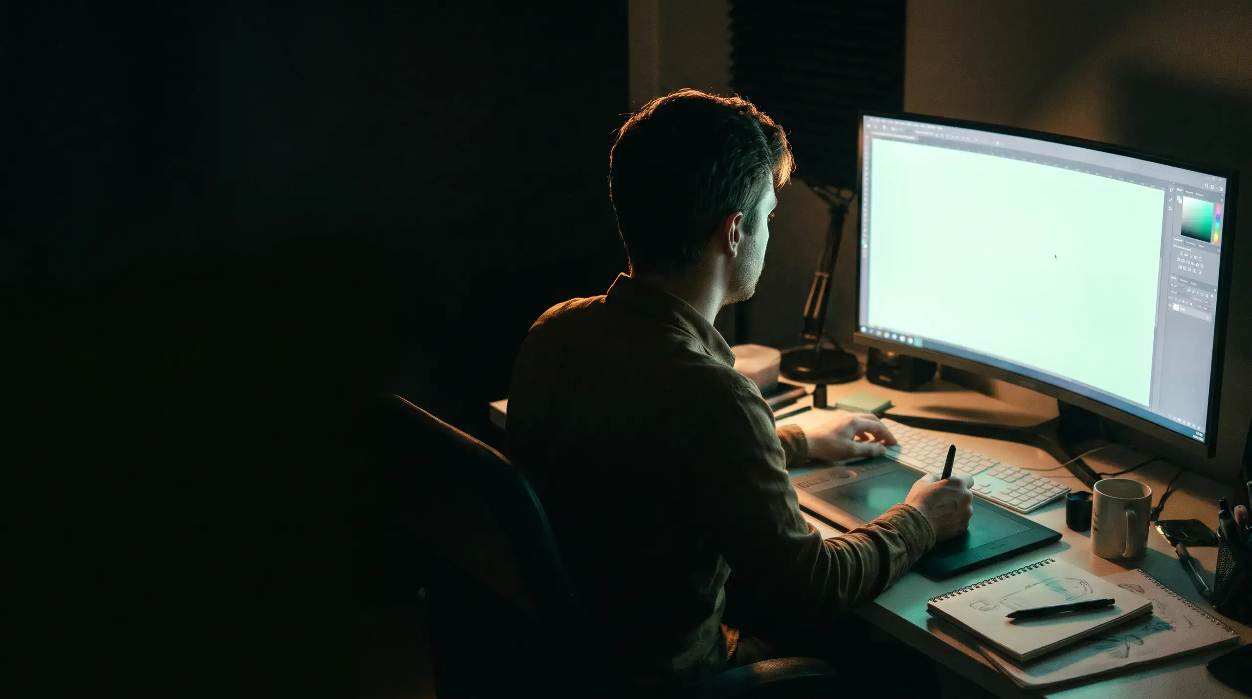 Un designer travaillant tard sur un grand écran, une tablette graphique à la main.