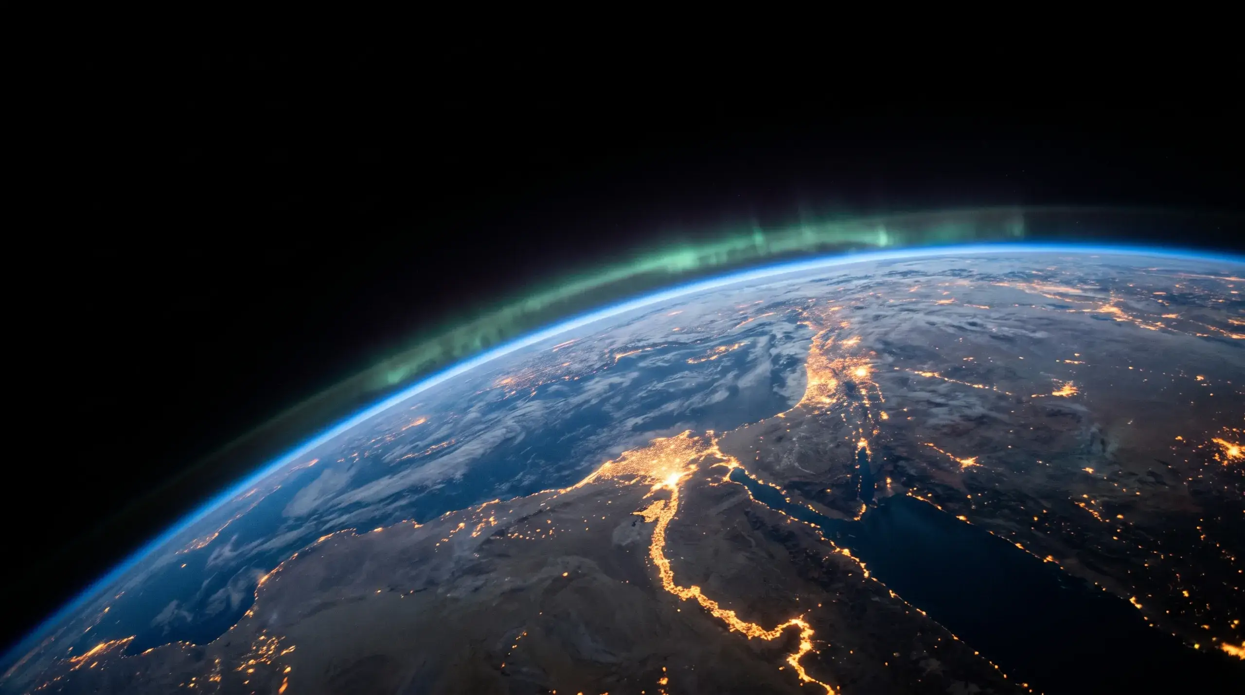 La Terre de nuit vue depuis l'orbite, les lumières des villes soulignant les côtes.